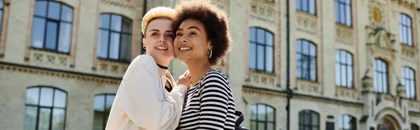 Duas jovens mulheres elegantes, um casal lésbico multicultural, posando em frente a um prédio universitário. — Fotografia de Stock