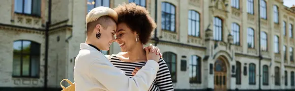 Two young women in stylish attire sharing a warm hug in front of an old building on a university campus. — Stock Photo