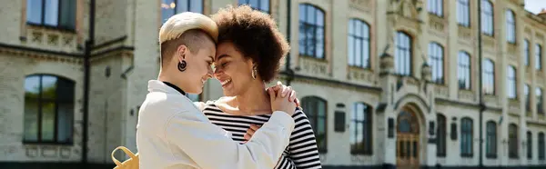 Two young women in stylish attire sharing a warm hug in front of an old building on a university campus. — Stock Photo