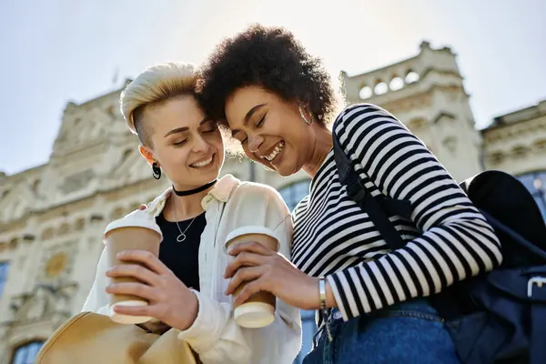 Zwei Frauen in legerer Kleidung lächeln einander an, während sie Kaffeetassen in der Hand halten. — Stockfoto