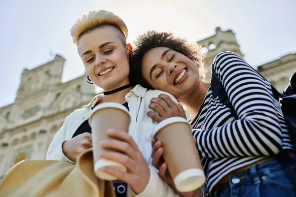 Zwei Mädchen in trendigen Outfits mit Kaffeetassen vor einem Universitätsgebäude. — Stockfoto