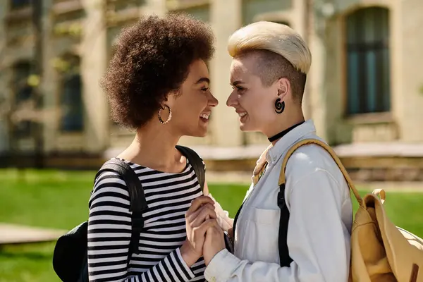 Two young women in stylish attire stand in front of a modern building on a university campus. — Stock Photo