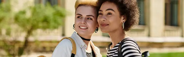 Un couple de lesbiennes multiculturel en tenue élégante se tient devant un bâtiment sur un campus universitaire. — Photo de stock