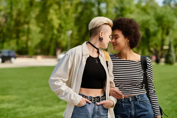 A multicultural lesbian couple, both young female students, stroll stylishly in a park near the university campus. — Stock Photo