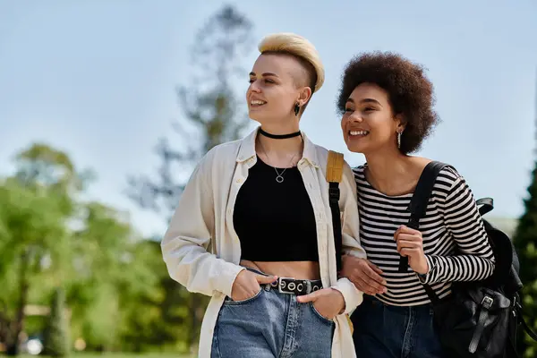 Deux jeunes femmes, un couple lesbien multiculturel, marchant ensemble dans un parc — Photo de stock