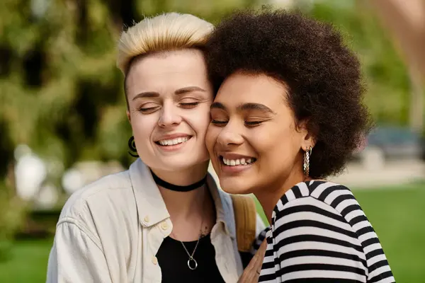 Two young women in stylish attire sharing a heartfelt hug in a vibrant park setting. — Stock Photo