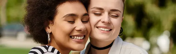 Two young women, a multicultural lesbian couple, sharing a moment of joy as they smile at each other in a sunny park. — Stock Photo