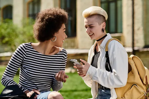 Dos mujeres jóvenes en un parque, absortas en llamadas telefónicas separadas, conectadas con seres queridos o amigos. - foto de stock
