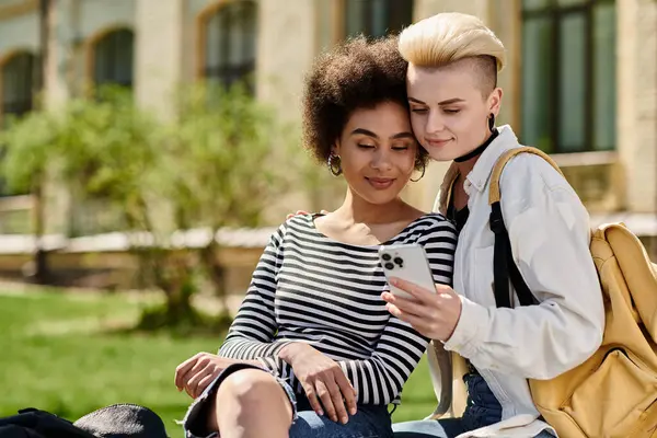 Lesbian couple in casual outfits sit on the grass, engrossed in phone, chatting and sharing moments. — Stock Photo