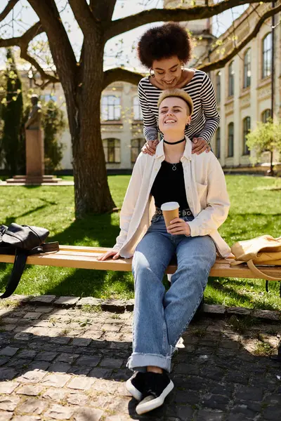 Deux jeunes femmes, vêtues avec désinvolture, s'assoient sur un banc dans un parc, profitant l'une de l'autre en compagnie d'une journée paisible. — Photo de stock