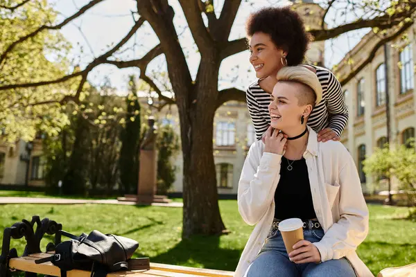 Two young female friends in casual attire sit on a park bench, enjoying each others company on a sunny day. — Stock Photo