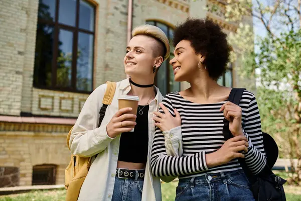 Multicultural lesbian couple, young female students, stand in front of a building on a university campus. — Stock Photo