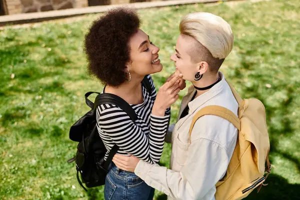 Two young women, dressed stylishly, share a heartfelt hug and kiss in a field of grass. — Stock Photo