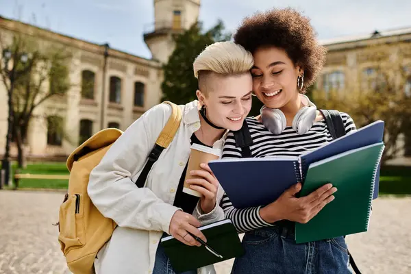 Deux jeunes femmes englouties dans un livre devant un immeuble sur un campus universitaire. — Photo de stock