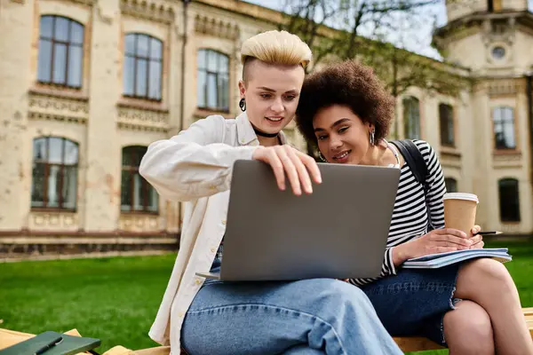 Two stylish young women sit together on a bench, focused on a laptop screen in front of them. — Stock Photo