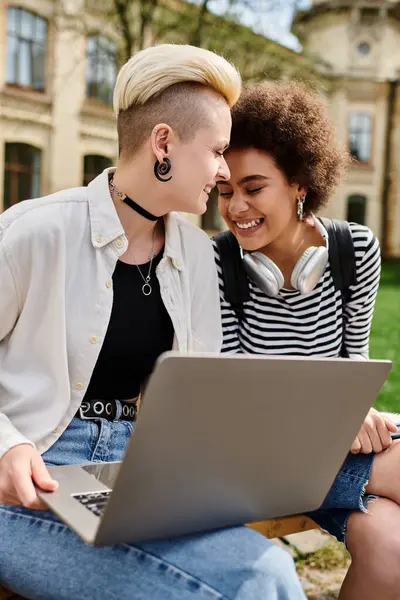 Duas mulheres em traje casual sentadas em um banco, focadas em uma tela de laptop. — Fotografia de Stock