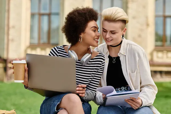 Two young women in casual attire sit on grass, looking at a laptop screen intently. — Stock Photo