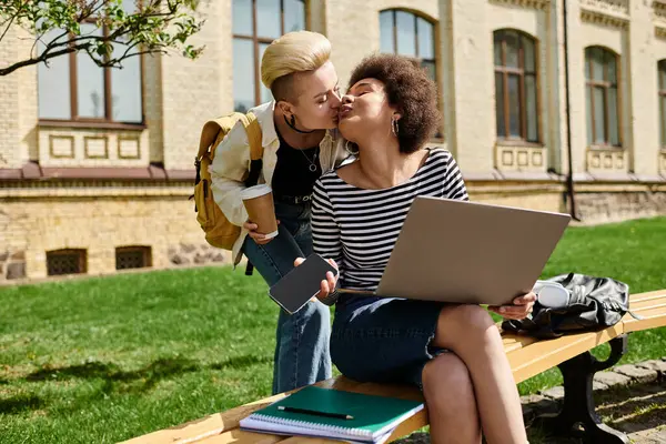 Two young girls passionately kissing while sitting on a bench with a laptop nearby. — Stock Photo