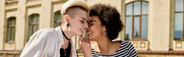 Due giovani donne multiculturali, vestite con stile, si abbracciano in un tenero bacio in una strada della città vicino a un campus universitario. — Foto stock