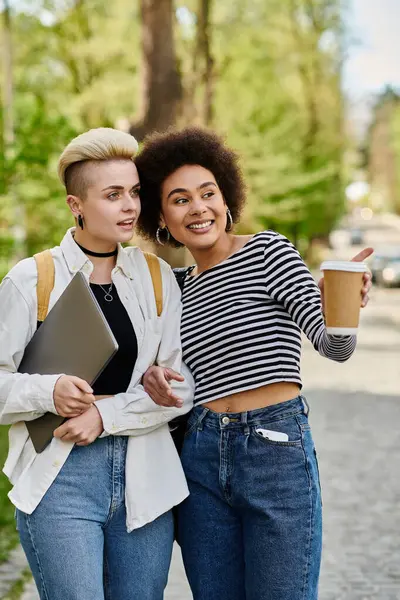 Дві молоді мультикультурні жінки в стильному вбранні стоять на тротуарі, тримаючи чашки кави. — стокове фото
