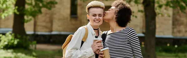 Un moment d'amour partagé entre deux jeunes femmes marchant dans un parc, échangeant un baiser sincère. — Photo de stock