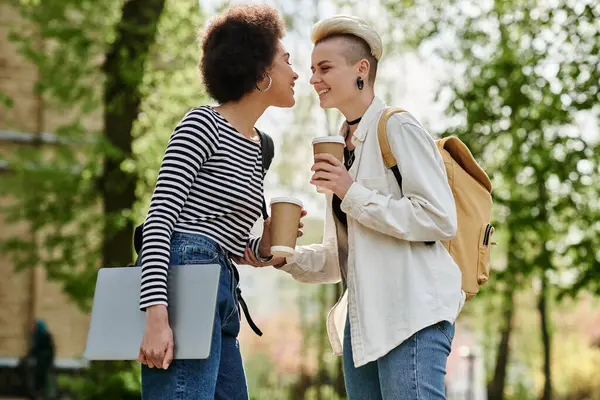 Two young women in casual attire chat over coffee and a laptop. — Stock Photo