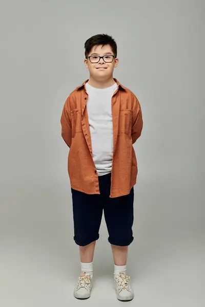 Маленький хлопчик з синдромом Дауна в окулярах і шортах, впевнено стоїть на сірому фоні. — стокове фото