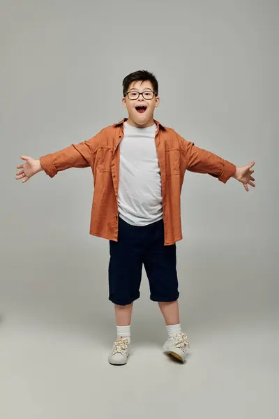 Little boy with Down syndrome, arms outstretched, against gray background. — Stock Photo