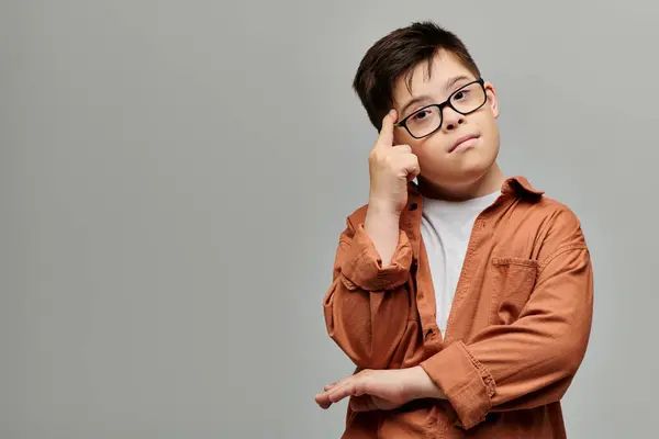 Adorable chico con síndrome de Down posando pensativamente con la mano en la cabeza. - foto de stock