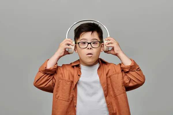 Um menino com síndrome de Down com óculos mergulha na música através de fones de ouvido. — Fotografia de Stock