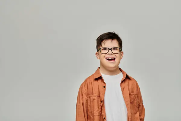 Ein kleiner Junge mit Down-Syndrom und Brille steht vor grauem Hintergrund. — Stockfoto
