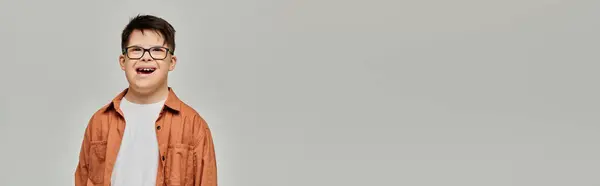 Little boy with Down syndrome in glasses stands against gray backdrop. — Stock Photo