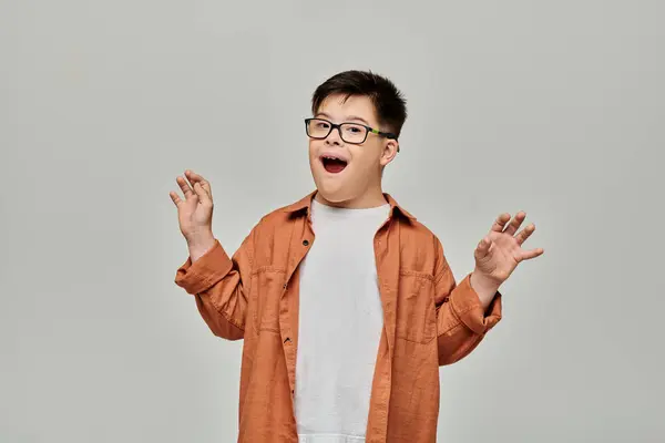 A boy with Down syndrome in glasses holds his hands up against a plain gray background. — Stock Photo