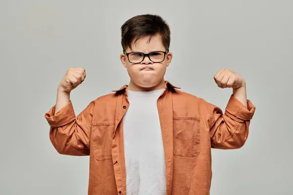 Um menino com síndrome de Down com óculos flexiona seus músculos, mostrando sua força e determinação. — Fotografia de Stock
