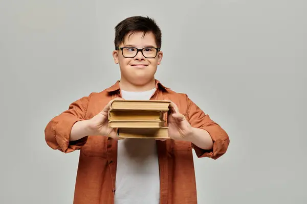Un ragazzo con la sindrome di Down tiene felicemente una pila di libri su uno sfondo grigio. — Foto stock