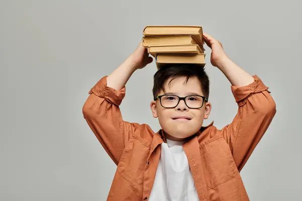 Niño pequeño con síndrome de Down balanceo pila de libros en la cabeza. - foto de stock