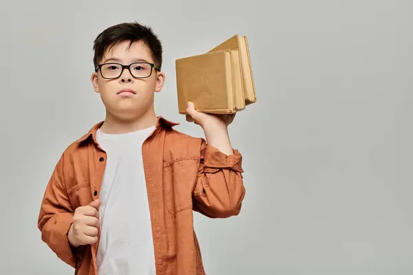 Petit garçon trisomique tenant une pile de livres. — Photo de stock