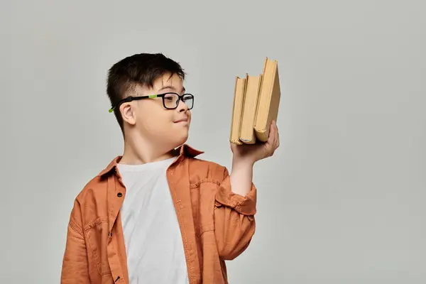 Un niño pequeño con síndrome de Down sostiene una pila de libros en su cara. - foto de stock