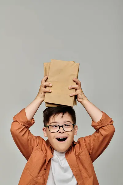 Симпатичный мальчик с синдромом Дауна игриво держит стопку книг. — стоковое фото