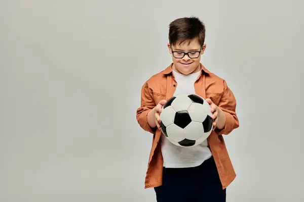 Мальчик с синдромом Дауна в очках держит футбольный мяч — стоковое фото