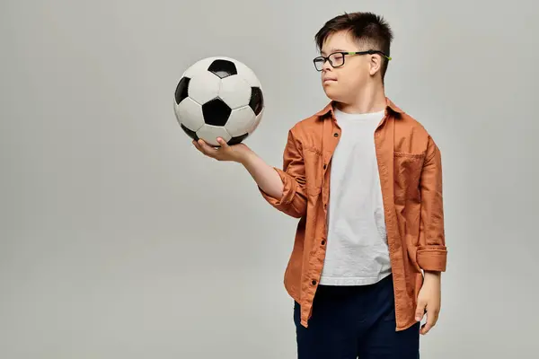 Menino com síndrome de Down com óculos segurando uma bola de futebol. — Fotografia de Stock