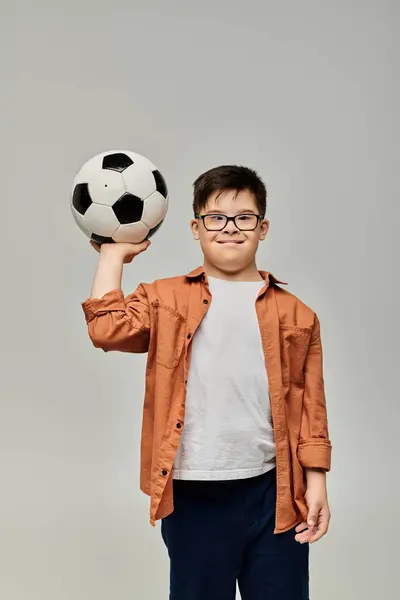 A little boy with Down syndrome holds a soccer ball on plain backdrop. — Stock Photo