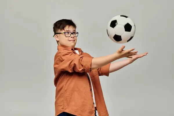 A charming boy with Down syndrome balances a soccer ball on a grey background. — Stock Photo
