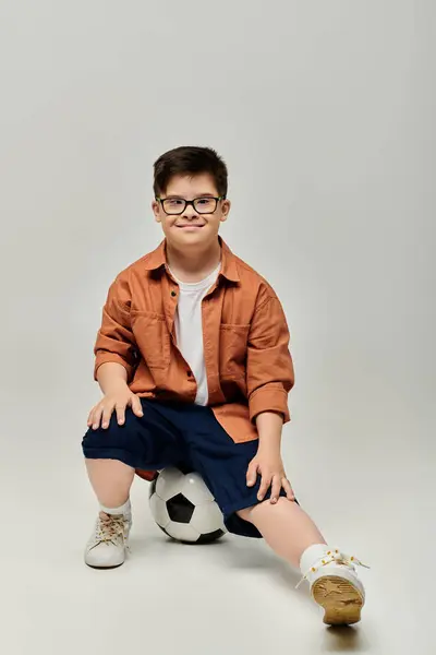 Симпатичный мальчик с синдромом Дауна в очках, позирующий с футбольным мячом. — стоковое фото