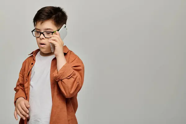 Niño pequeño con síndrome de Down con gafas charlando por teléfono. - foto de stock