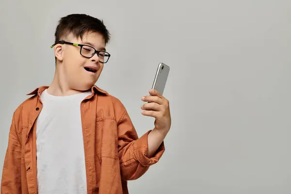Un ragazzo con la sindrome di Down con gli occhiali tiene un cellulare. — Foto stock
