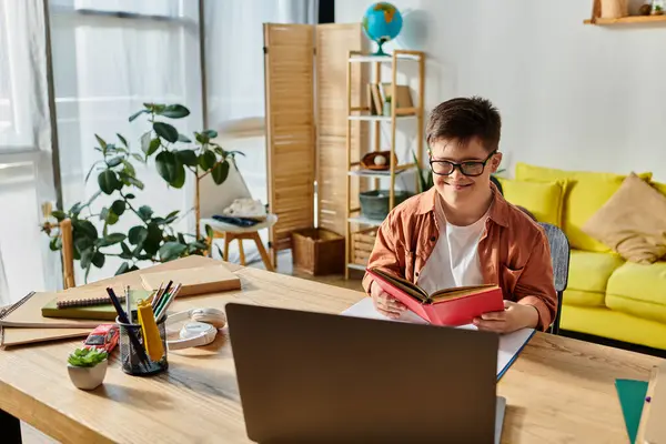 A adorable boy with Down syndrome absorbed in reading a book and using a laptop. — Stock Photo