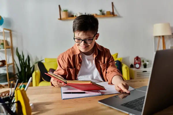 Adorable boy with Down syndrome working on a laptop and reading a book at a table. — Stock Photo