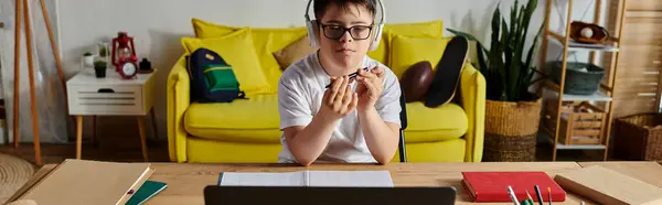 A boy with Down syndrome with glasses works on his laptop at a desk. — Stock Photo