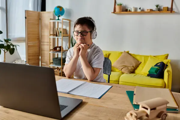 Adorable boy with Down syndrome wearing headphones, engrossed in using laptop at desk. — Stock Photo